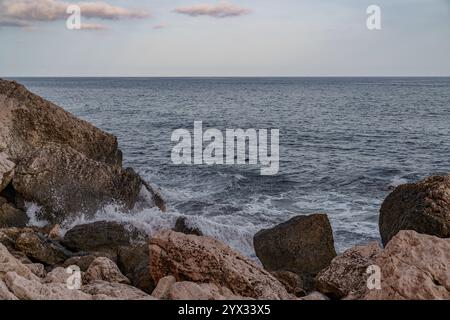 Il mare visto all'orizzonte da una spiaggia rocciosa con onde che si infrangono sulla riva Foto Stock