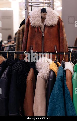 Morbidi cappotti in pelliccia nera, marrone e blu, capospalla invernali appesi in fila su grucce in una boutique di lusso alla moda Foto Stock