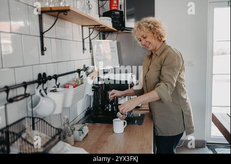 Donna matura sorridente che prepara il caffè in cucina. Foto Stock