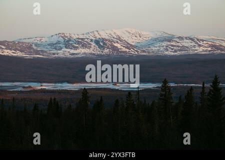 Uno splendido paesaggio nordico invernale caratterizzato da montagne innevate e un bacino artificiale ghiacciato, circondato da una fitta foresta. Foto Stock