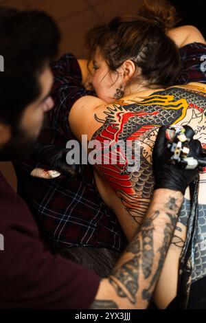 Tatuatore che fa tatuaggio tradizionale giapponese sulla schiena della donna Foto Stock