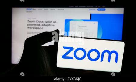 In questa immagine, una persona ha in mano uno smartphone con il logo della società di comunicazioni statunitense Zoom Video Communications Inc. Davanti al sito Web. Foto Stock