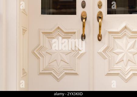 Porta bianca con maniglie in ottone e intricati dettagli a forma di stella intagliati Foto Stock