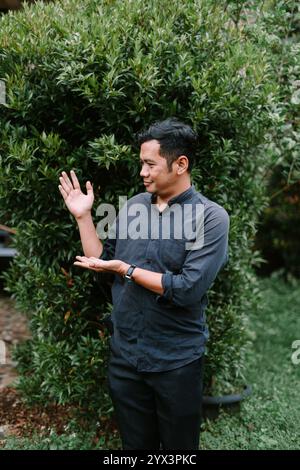 Un uomo del sud-est asiatico che punta a qualcosa nella sua mano, evidenziando l'oggetto con interesse. Perfetto per dimostrazioni di prodotti, stile di vita o inst Foto Stock