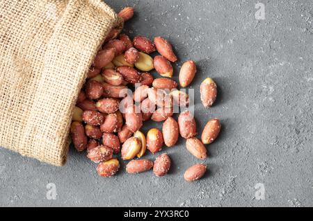 Arachidi salate arrostite senza guscio nel recipiente o sacco di bavaglio su fondo rustico, concetto di noci Foto Stock