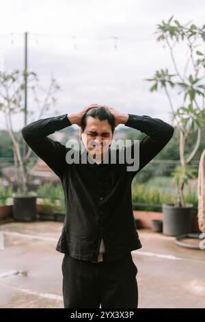 Un uomo del sud-est asiatico che tiene la testa nel dolore, mostrando segni di disagio. Perfetto per progetti di salute, medici o di stile di vita che descrivono difficoltà o Foto Stock