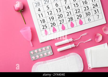 Composizione piatta con calendario e prodotti mestruali su sfondo rosa Foto Stock