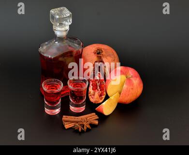 Liquore di melograno di mela su sfondo nero, una bottiglia e due bicchieri con alcol fatto in casa, cannella e anice. Primo piano. Foto Stock