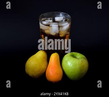 Mescolare il succo di mela e pera con il ghiaccio in un bicchiere alto su sfondo nero, frutta matura nelle vicinanze. Primo piano. Foto Stock