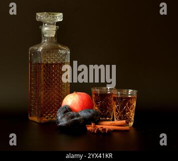 Liquore prugna-mela con cannella e anice su sfondo nero, forte alcol fatto in casa con spezie e in cristalleria. Primo piano. Foto Stock