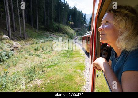 Giovane donna sorridente che si gode la vista dalla finestra del treno storico rosso al ghiacciaio Mer de Glace a Chamonix. Francia Foto Stock