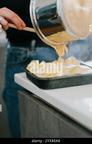Una persona sta cucinando il cibo in una padella su un piano cottura. La padella è riempita con una salsa cremosa e la persona la sta versando in un piatto Foto Stock