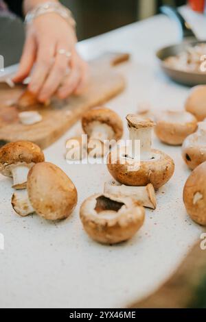 Una persona sta tagliando i funghi su un tagliere. I funghi sono in varie fasi di preparazione, con alcuni già tagliati e altri ancora interi. Co Foto Stock