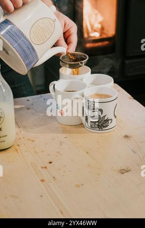 Una persona sta versando il caffè in quattro tazze. Le tazze sono disposte su un tavolo di legno Foto Stock