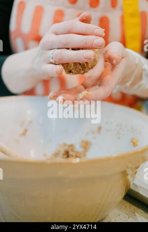 Una donna sta preparando una pasta per biscotti con le mani. Sta indossando un grembiule giallo. L'impasto è in una ciotola Foto Stock