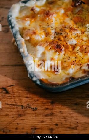 Su un tavolo di legno si trova un piatto di formaggio. Il piatto è ricoperto di formaggio e presenta una spolverata di pepe Foto Stock