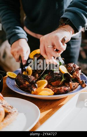 Una persona sta tagliando un pollo arrosto con un coltello e una forchetta. Il pollo viene servito su un piatto blu con fette d'arancia Foto Stock