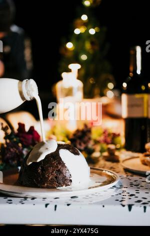 Un dessert bianco e marrone viene versato su un piatto. Il dessert è un tipo di torta, e il latte viene versato sopra di esso. La scenografia è impostata in un din Foto Stock