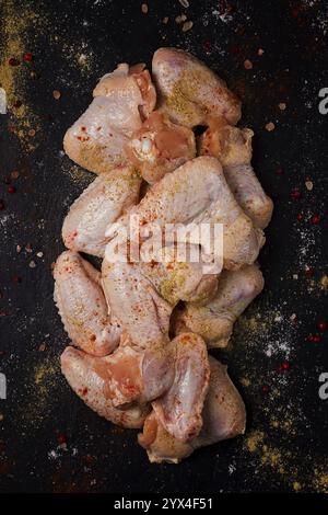 Ali di pollo crude fresche, con spezie, su sfondo nero Foto Stock