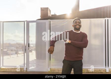 Foto frontale di tre quarti di lunghezza di un uomo africano felice in abiti casual che ballano gratis in città in una giornata di sole Foto Stock