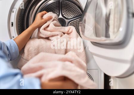 le mani femminili scaricano il bucato, prelevando un asciugamano di cotone pastello dalla lavatrice con porta aperta Foto Stock