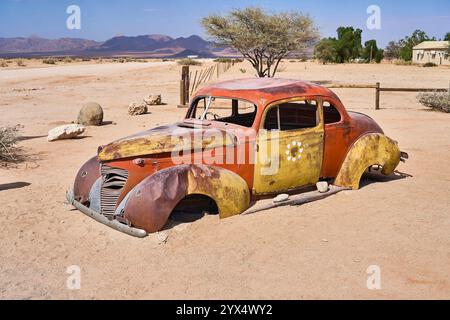 Un vecchio temporizzatore arrugginito, un'auto con orrange e parti di colore giallo, senza finestrini o pneumatici, relitti di auto di Solitare, Namibia Foto Stock