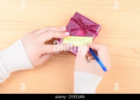 Una giovane donna che scrive una nota di ringraziamento su una confezione regalo. Concetto di vacanza. Foto Stock