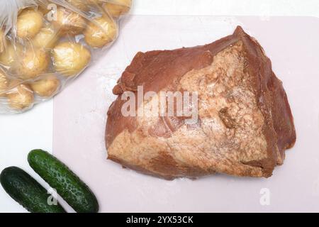 Carne marinata su un tagliere, patate neonate in un sacchetto e cetrioli. Cucina casalinga. Foto Stock