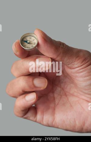 primo piano della mano che tiene la piccola bussola rotonda vintage sfondo grigio isolato, quadrante bianco con marcature per direzioni e punti cardinali Foto Stock