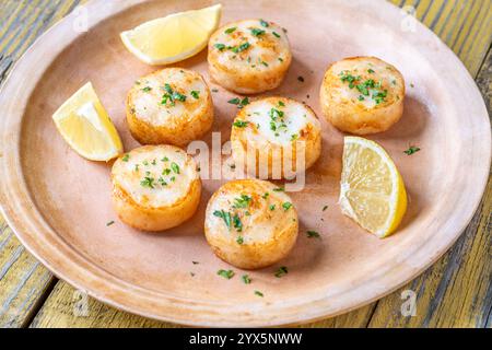 Morbide capesante fritte in burro servite con limone, prezzemolo, rustico fondo giallo Foto Stock