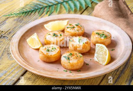 Morbide capesante fritte in burro servite con limone, prezzemolo, rustico fondo giallo Foto Stock