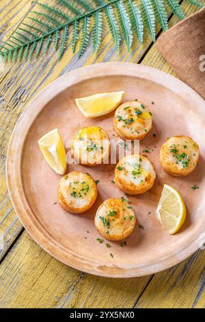 Morbide capesante fritte in burro servite con limone, prezzemolo, rustico fondo giallo Foto Stock