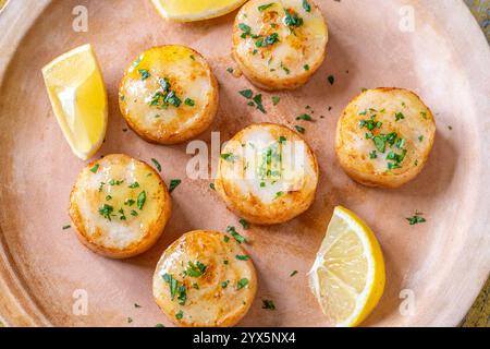 Morbide capesante fritte in burro servite con limone, prezzemolo, rustico fondo giallo Foto Stock
