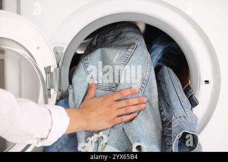 Donna che mette jeans sporchi e altri vestiti in denim in lavatrice, primo piano Foto Stock