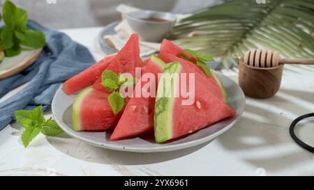 Fette di anguria disposte su un piatto, guarnite con foglie di menta e un cucchiaio di miele nelle vicinanze. Foto Stock