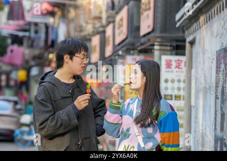 Giovane coppia cinese sui 20 anni che mangia i famosi dolci di frutta ricoperti di zucchero di Pechino su un marciapiede nel quartiere di Hongkou, Shanghai, Repubblica Popolare di Foto Stock
