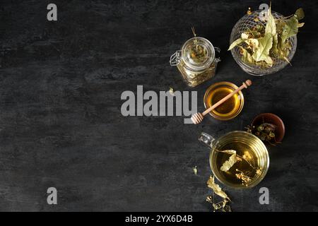 Tazza di gustoso tè al tiglio, miele e barattolo con foglie su sfondo nero Foto Stock