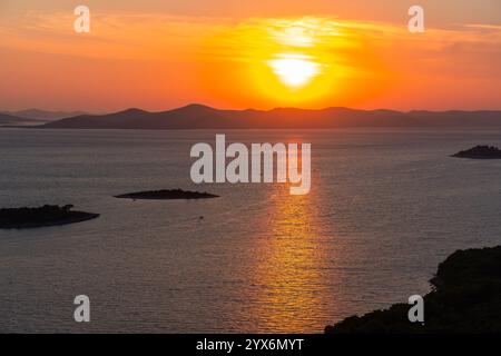 Tramonto dorato sul mare calmo con riflessi luminosi e sagome di piccole isole e colline lontane. Concetto di natura tranquilla, romantico paesaggio marino Foto Stock