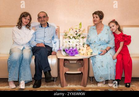 Due nipoti si siedono con i loro nonni russi, per celebrare il loro 50 ° anniversario di matrimonio d'oro. La famiglia è seduto su un divano, circondato Foto Stock