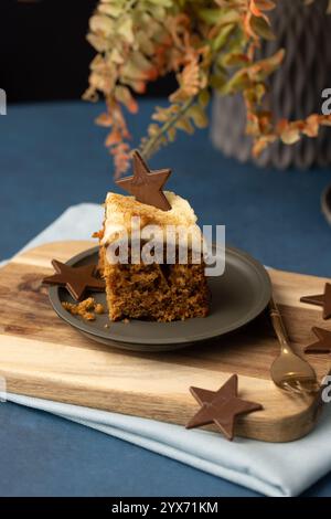 Un pezzo di torta di carote placcata fotografato da una posizione leggermente rialzata. Il piatto è su un tavolo e la torta è arrotondata da stelle di cioccolato. Foto Stock