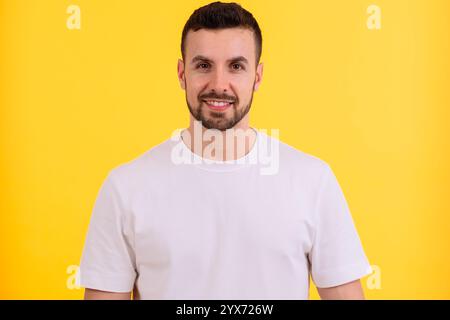 Uomo sorridente con una camicia bianca in posa su un vivace sfondo giallo. Foto Stock