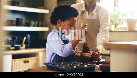 Cuocere, imparare e bambino con la madre in cucina per sviluppare le proprie abilità con i cupcake al cioccolato. Insegnare, legare e cucinare biscotti per bambini Foto Stock