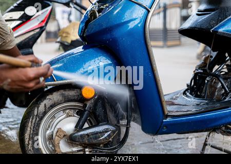 Risciacquo rinfrescante! Uno scooter blu viene pulito a fondo con un getto d'acqua, scintillante sotto il sole. Foto Stock