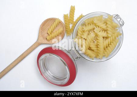 Pasta, varietà "Fusili" in contenitore di vetro con cucchiaio da cucina Foto Stock