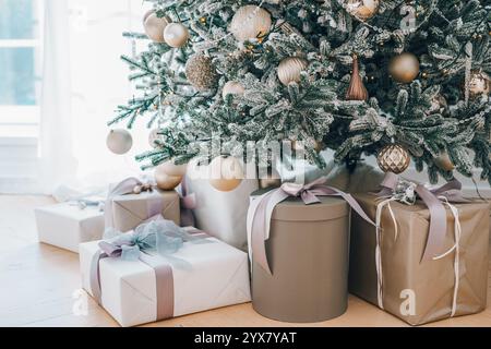 L'albero di Natale decorato sorge in un soggiorno illuminato dal sole, adornato con ornamenti dorati e luci scintillanti. Regali confezionati, scatole regalo sotto Christma Foto Stock