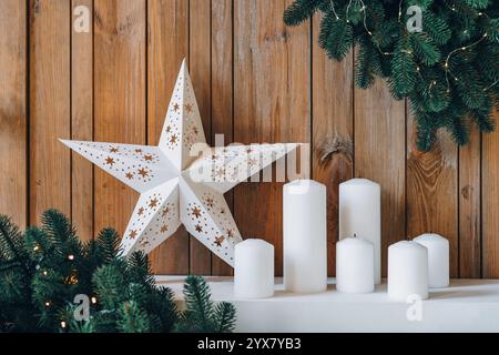 Decorazioni natalizie con stella bianca, candele e ghirlande sempreverdi su sfondo in legno. Decorazioni ben arredate con grande stella bianca e candele Foto Stock