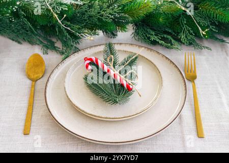 Decorazioni natalizie. Tavolo da pranzo splendidamente organizzato, eleganti piatti bianchi, posate dorate e ghirlanda di abete su tovaglia bianca, creando un holi festoso Foto Stock