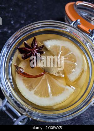 Vista dall'alto di appetitose fette di limone in un vaso di vetro, in marinata. In cima - stelle di anice, peperoncino e alloro Foto Stock