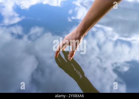 Womans aveva toccando la superficie di un lago, riflessioni di mano e cielo Foto Stock