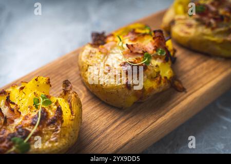 Patate al forno con formaggio e pancetta schiacciate su un asse di legno su un tavolo grigio. Foto di alta qualità Foto Stock